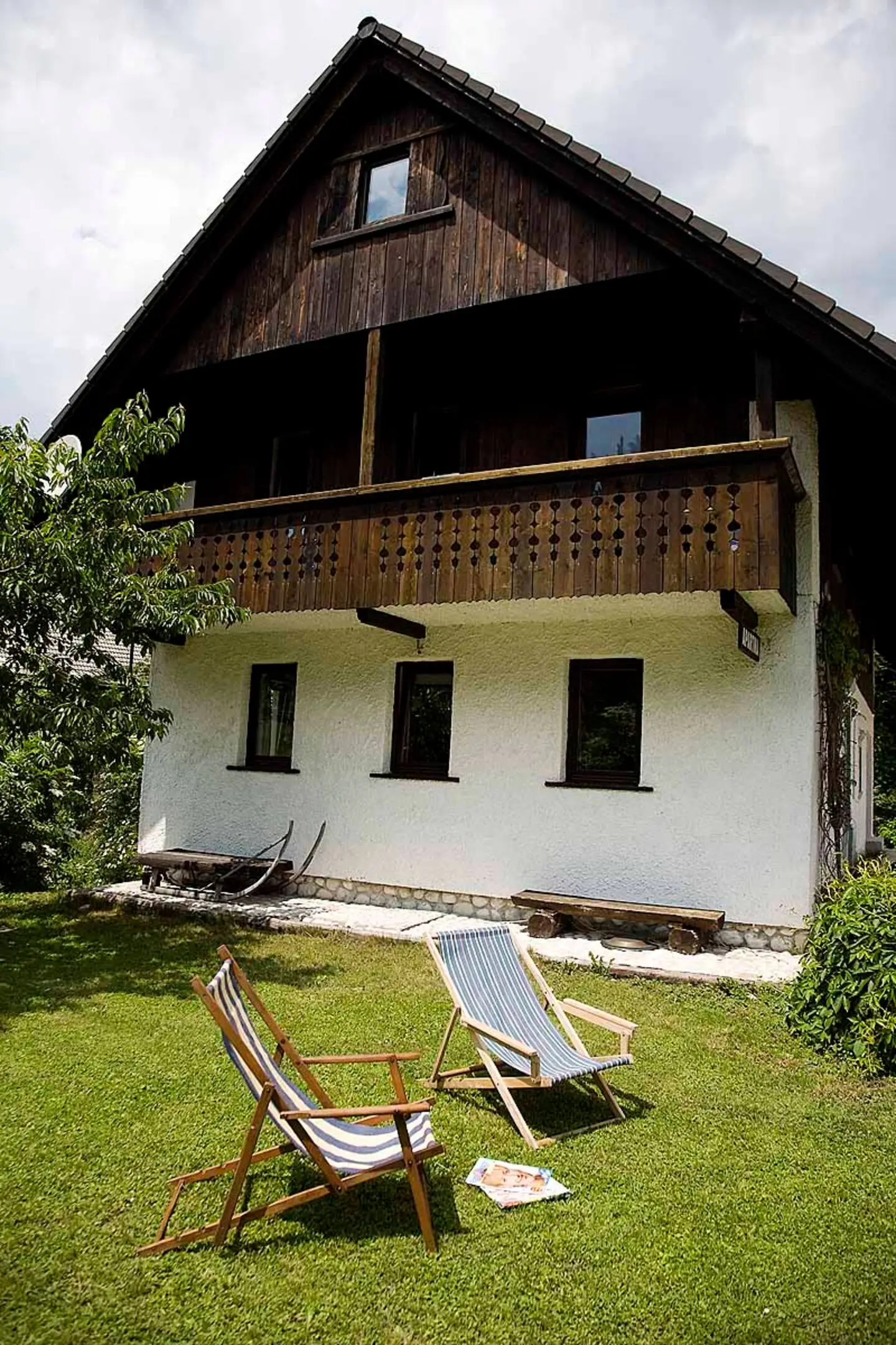 Hiša z dolgim lesenim balkonom, pred njo ležalnika na travi