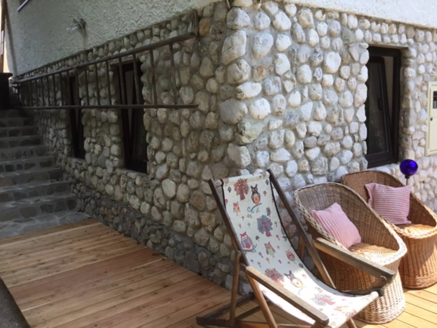 Terasa s pletenimi stoli pred vhodom v spodnji apartma, ob kamnitem zidu